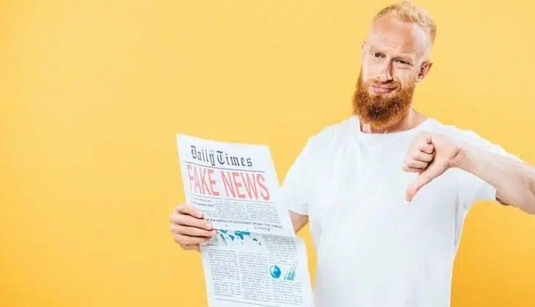 uomo in t-shirt bianca legge giornale dal titolo "Fake news" e mostra il pollice verso